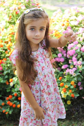 A vertical shot of a caucasian little girl in a floral dress with a flower in her hand