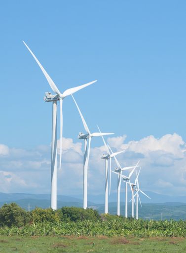 A vertical shot of wind turbines with green mountains in the background