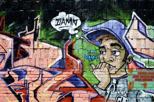 A multi color graffiti on brick wall, young men biting fingers, thought bubble with the word DAMN
