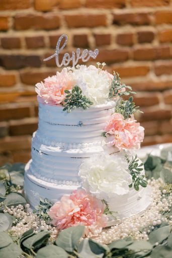 A vertical shot of a three-layered wedding cake topped with love text