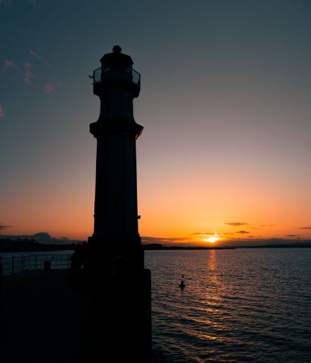 A beautiful sunset over the sea with a silhouette of a lighthouse