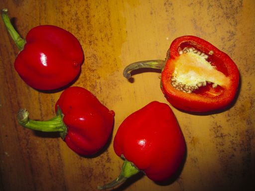 A close up shot of red bell peppers cut and uncut on a wooden table