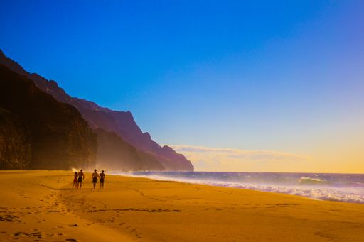 A beautiful shot of people walking on the beach shore near the mountains with a blue sky in the background