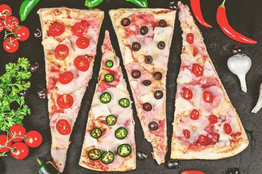 A close-up of a variety of freshly baked pizza slices with colorful toppings of red peppers, tomatoes, and black olives arranged on a table
