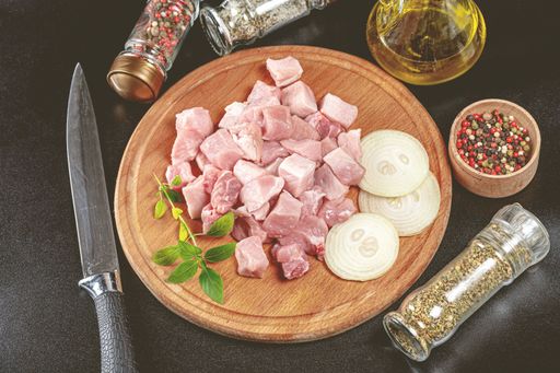 A cutting board displaying a variety of fresh ingredients, including pieces of raw meat, herbs and spices