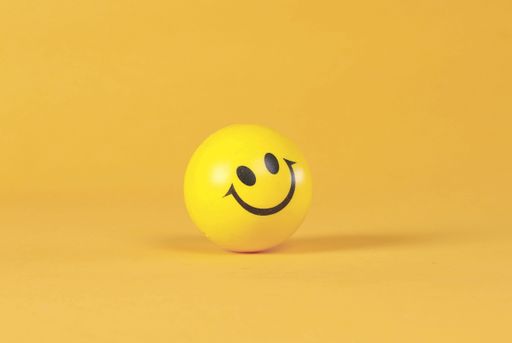 A cheerful yellow smiley face ball against a vibrant orange background