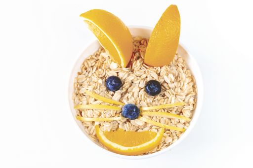 A top view of a bowl of oatmeal decorated with fresh fruit in the shape of a bunny isolated on a white background
