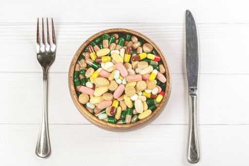 A top view of a bowl with colorful capsules and tablets on a wooden background