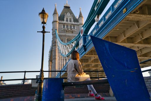 A woman sitting on the bench and looking at the Tower Bridge, shot from back