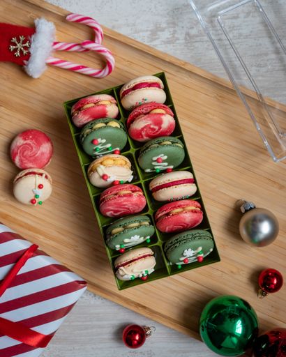 The vertical top view of colorful macarons in the box on a wooden surface - Christmas sweets
