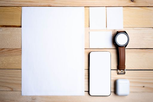 A closeup of blank white papers with a watch, and phone on a wooden surface.