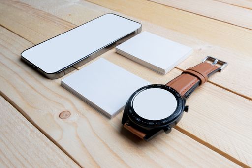 A closeup of blank white papers with a watch, and phone on a wooden surface.