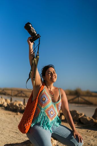 A vertical shot of an attractive woman with tattoos sitting on a rock with a camera in her hand