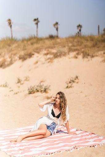 A vertical shot of a pretty lady lying down on a towel on a sandy beach
