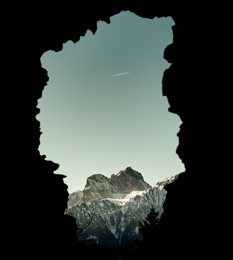 A scenic view of a plane flying over a cliff covered with snow seen from a cave