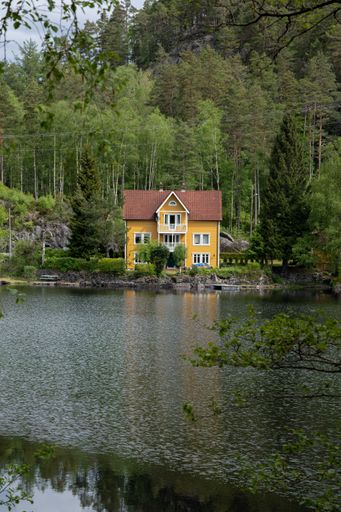 Wonderful landscapes in Norway. Vest-Agder. Beautiful scenery of a yellow villa reflecting in the lake. Wooden floating platform