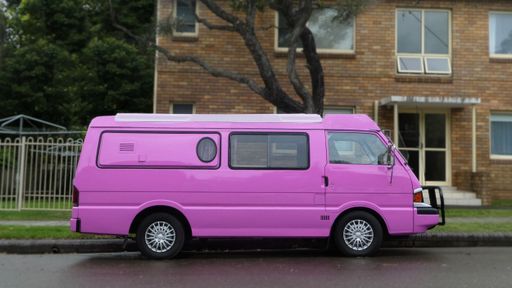 side view of pink camper van parked outdoors on street in front of building