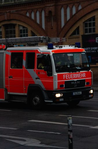 A closeup shot of an orange fire brigade vehicle, in the street in Berlin, Germany, with firefighters driving, and a brick building in the background