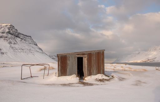 A small shack house surrounded by snowy mountains under a cloudy sky