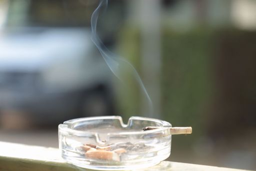 A closeup of an ashtray with a smoking cigarette.