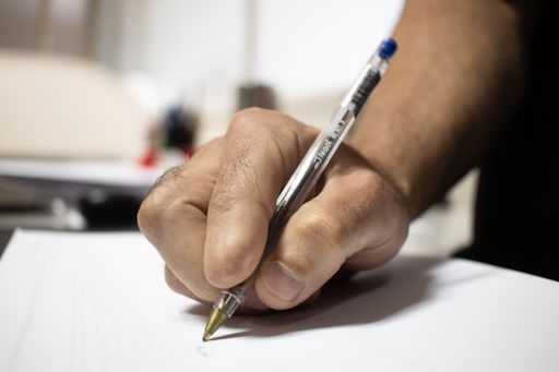 Hand with amputated index finger writing with a pen in a white paper.