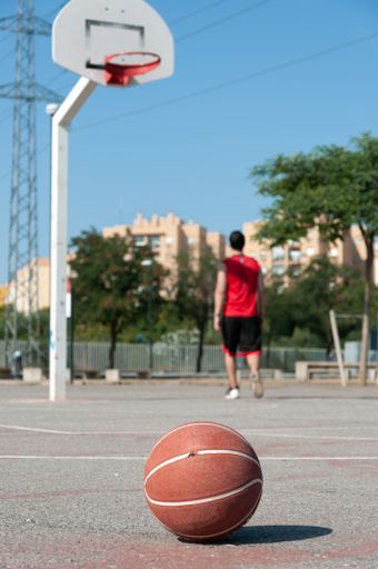 A vertical shot of a ball in a basketball court with a man on the background