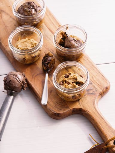 A vertical closeup of handmade cookie doughs in small glass jars on a wooden board
