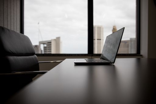 A selective focus shot of a laptop on the table and an empty chair