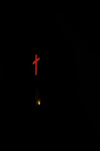 A vertical shot of a neon red cross at night