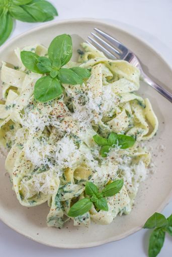 A closeup top view of Italian pasta Cheese and Pepper (Cacio e Pepe) served with basil leaves on white background