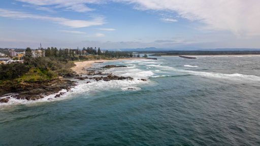 A scenic view of Town Beach in Port Macquarie, NSW, with thick green trees and buildings on the coast