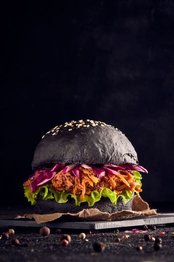 pulled pork belly burger with black bread in a dark background coleslaw and lettuce with onion