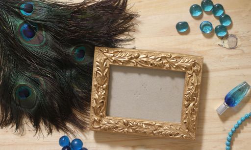 Blue Jewelry and Peacock Feathers With Gold Picture Frame on Wood Background