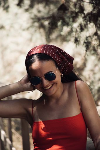 A shallow focus of a young female wearing a red top with sunglasses and a bandana laughing in a park
