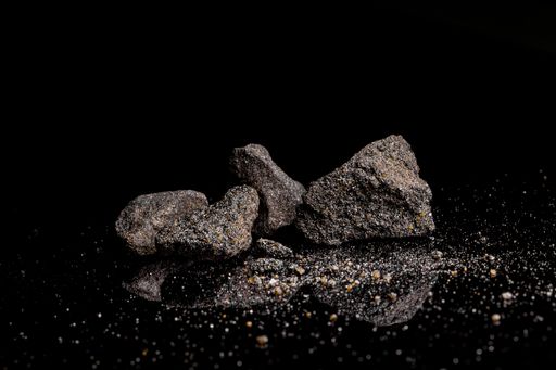 Macro Close up image of raw material Platinum and Chrome Ore rock isolated on black reflective background