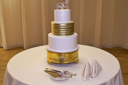 A wedding cake white and gold with ring topper