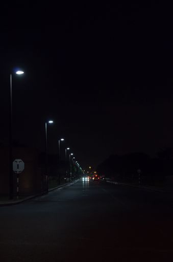 A vertical shot of lanterns and traffic lights illuminating an asphalt road at night in Muscat, Oman
