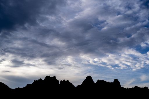 Mountain skyline on horizon. Dark silhouette of mountains against blue and dramatic sky with grey clouds. Outdoor adventure moutain landscape photo.