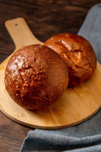 A vertical shot of a pair of sourdough bread on a circular wooden board