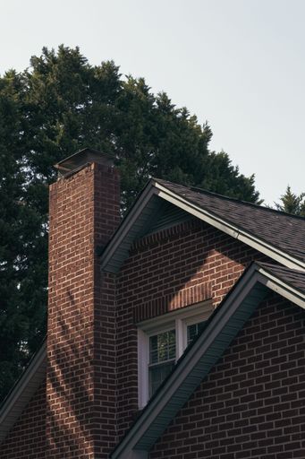A vertical shot of a brick house and a high tree under the white sky
