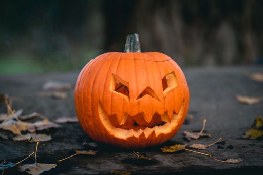 A selective focus closeup of a craved jack-o-lantern with fallen autumn leaves on the floor