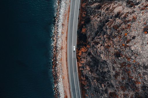 An aerial shot of a seashore with lots of rocks near the road