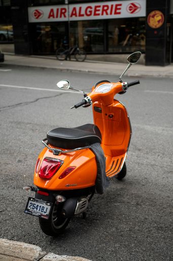 A vertical of an orange moped parked on a street in Montreal, Canada