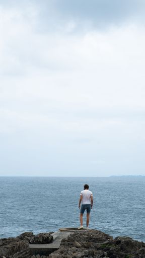 A vertical shot of a young Caucasian man admiring the seascape on a cloudy day