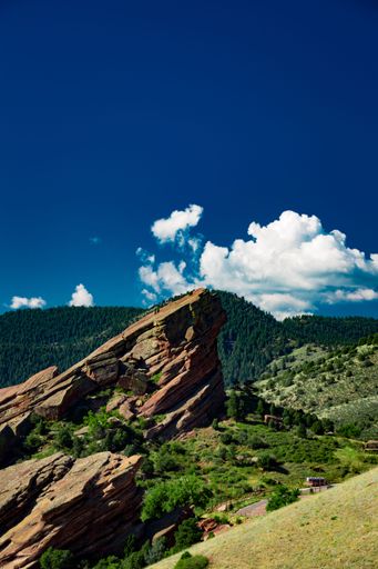A vertical shot of a rock against mountains covered with green forests under a cloudy blue sky