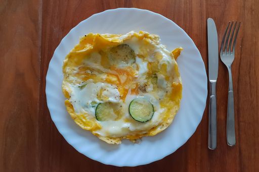 An overhead shot of a fried egg served in a white plate with fork and knife on its right side