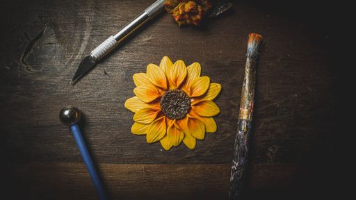 A top view of a sunflower made with polymer clay surrounded by craft tools