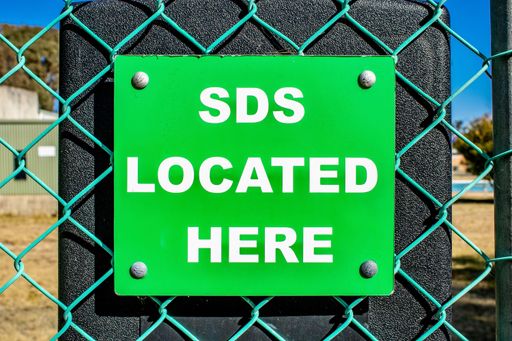 A closeup of green square SDS LOCATED HERE sign on turquoise mesh wire fence against black surface