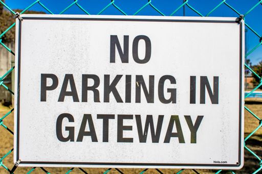 A closeup shot of a white "no parking" sign hung on a metal fence on a sunny day