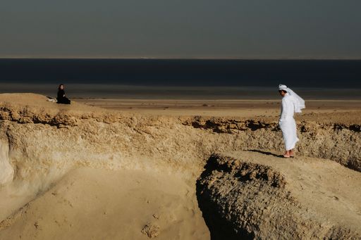 couple looking at each other in sand dunes rock formation in zekreet doha qatar